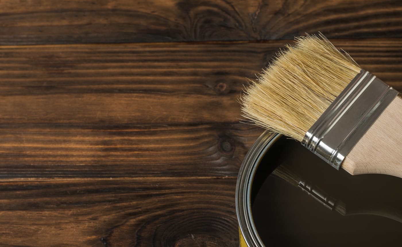 Brush on a tin with tinting composition on a wooden background. The rendering of wood.