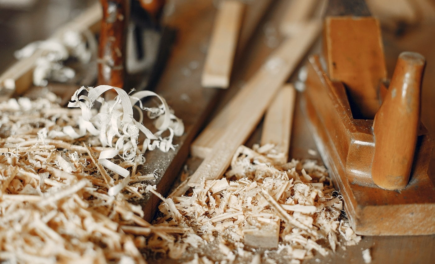 Man working with a wood. Carpenter in a white shirt. Man with a chisel