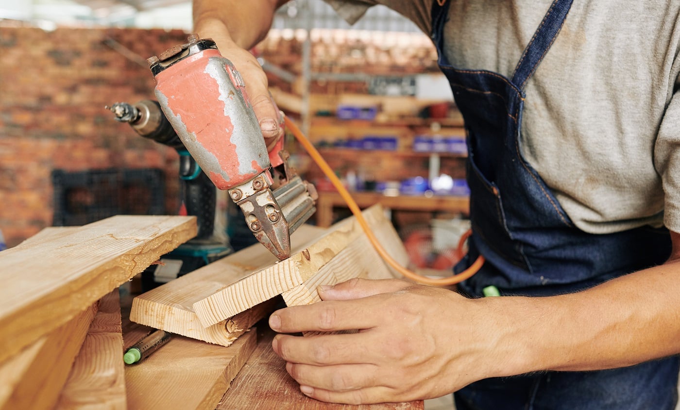 Close-up image of professional carpenter using staple gun when working with wood in his studio