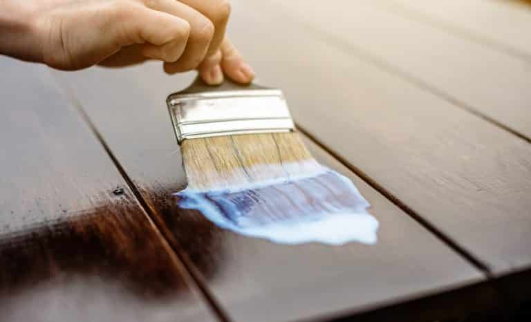 A wood carpenter applies a protective layer of transparent varnish. Hand with a brush close up on the table top