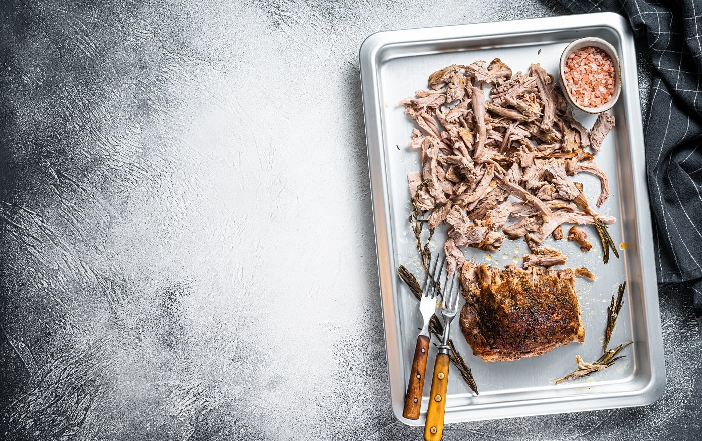 Texas bbq smoked puilled pork meat in a steel baking tray. White background. Top view. Copy space.