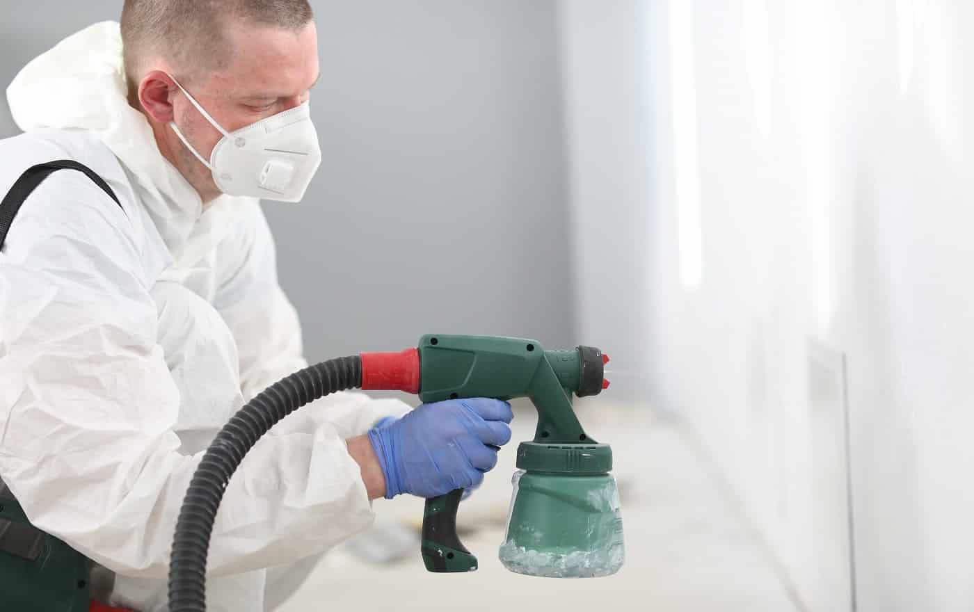 Man in mask holds spray gun in his hands and paints the wall. Courses on mastering new profession concept