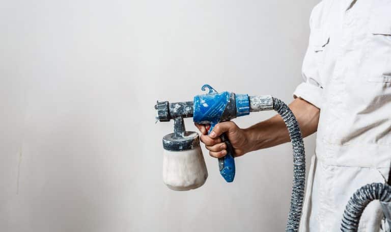 Worker painting wall with spray gun in white color. Copy space.