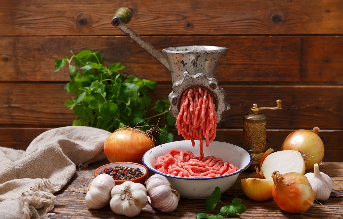 old meat grinder with minced meat and vegetables on wooden table