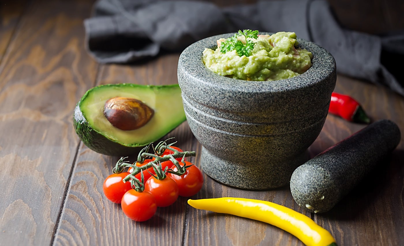 Traditional Mexican Guacamole sauce with avocado in a mortar or molcajete over dark wooden background