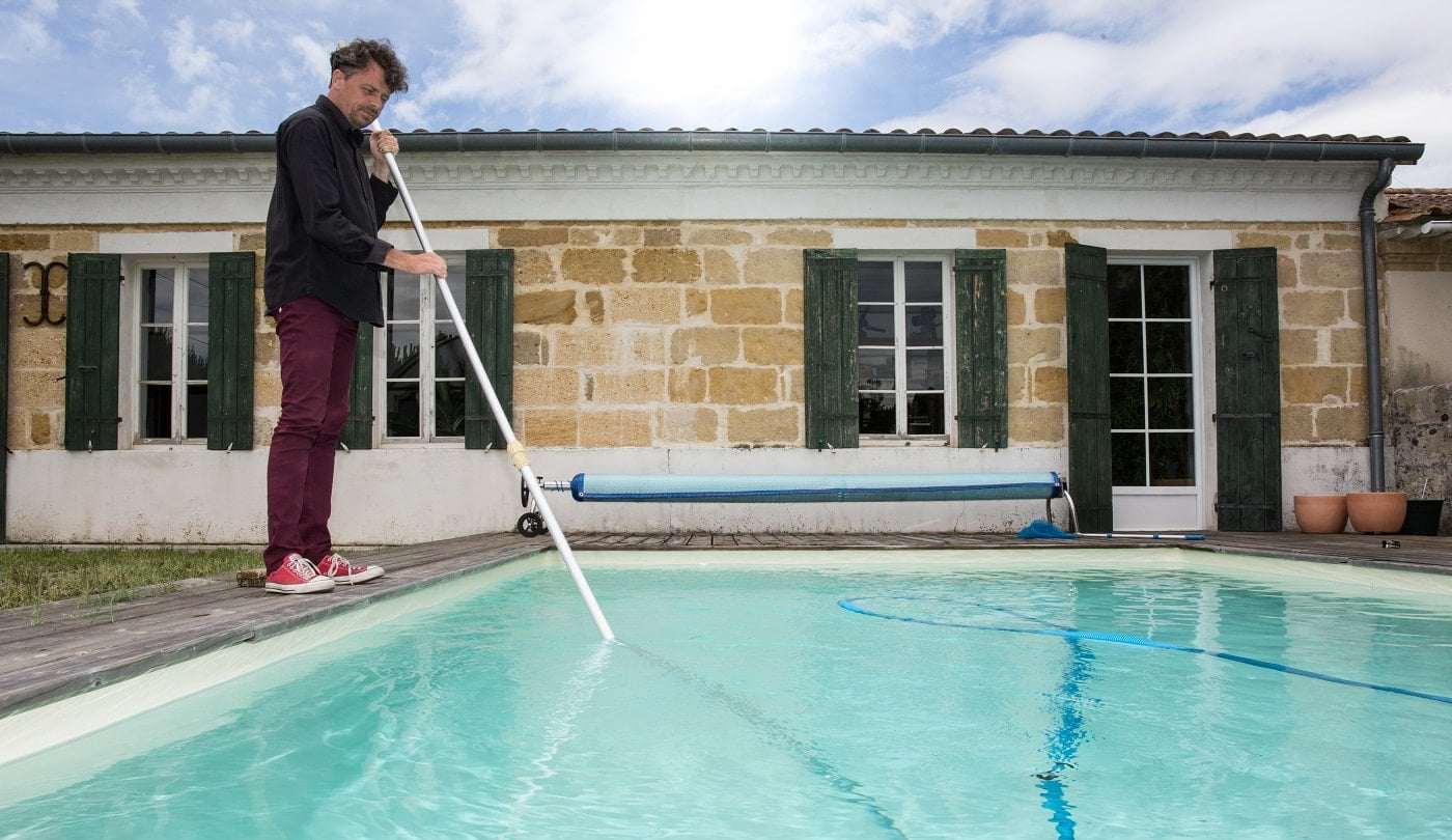 Man cleaning blue swimming pool with vacuum cleaner