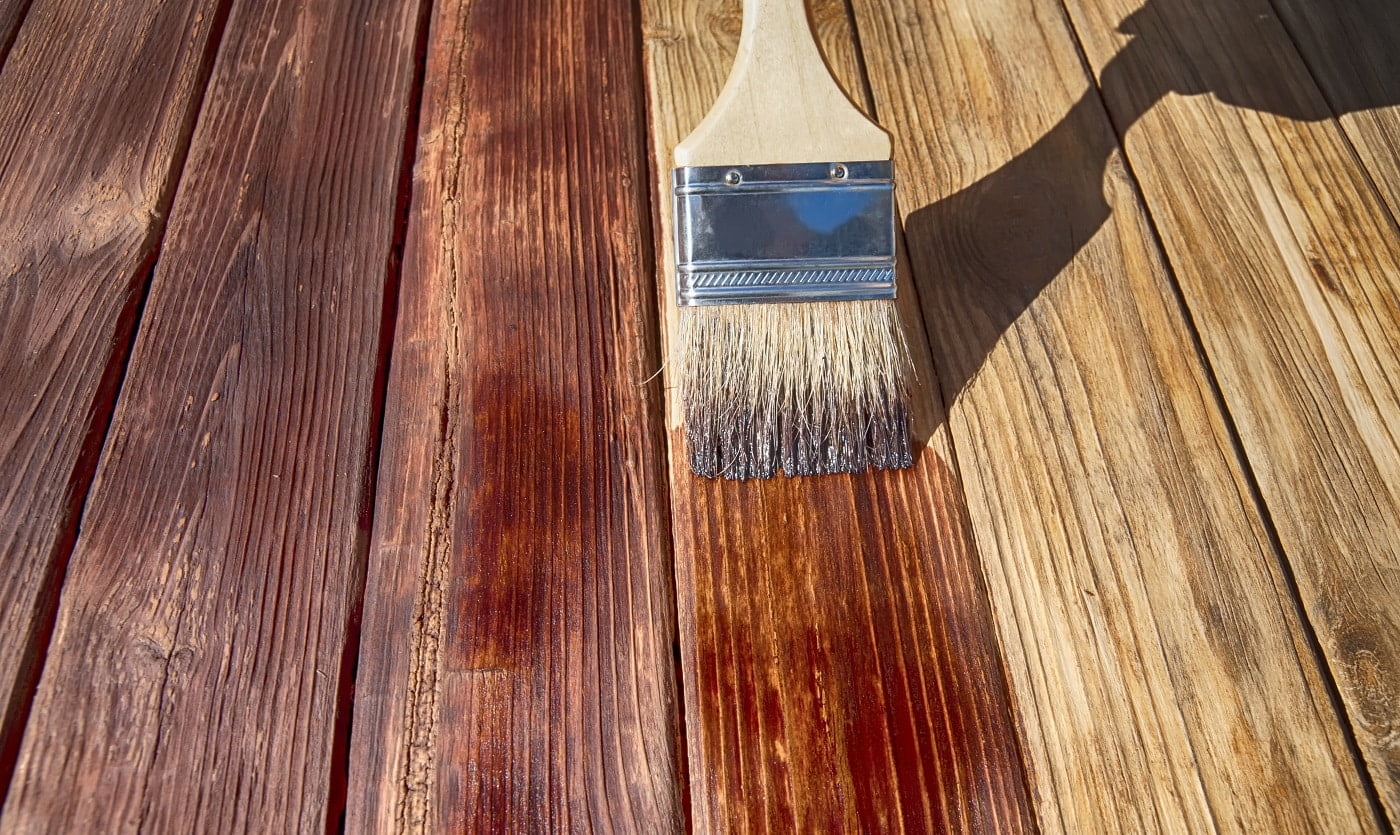 a wooden brush covers the wooden plank surface with a dark red stain front side view close up