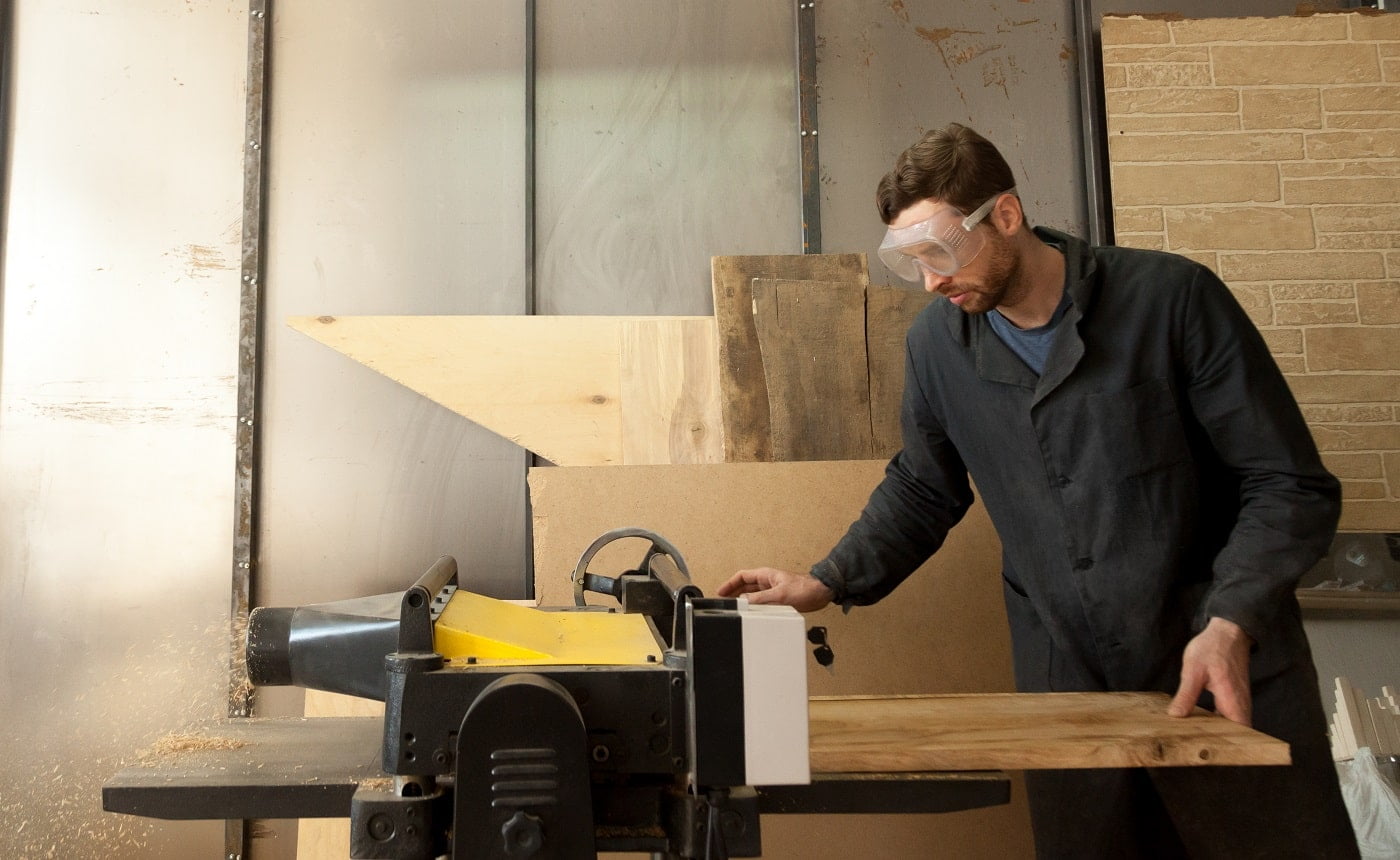 Carpenter trims massive wooden board on woodworking thickness planer machine. Joiner working at own small sawn timber manufacture. Young entrepreneur developing his local sawmill, furniture business. DeWalt DW735X Planer Verdict