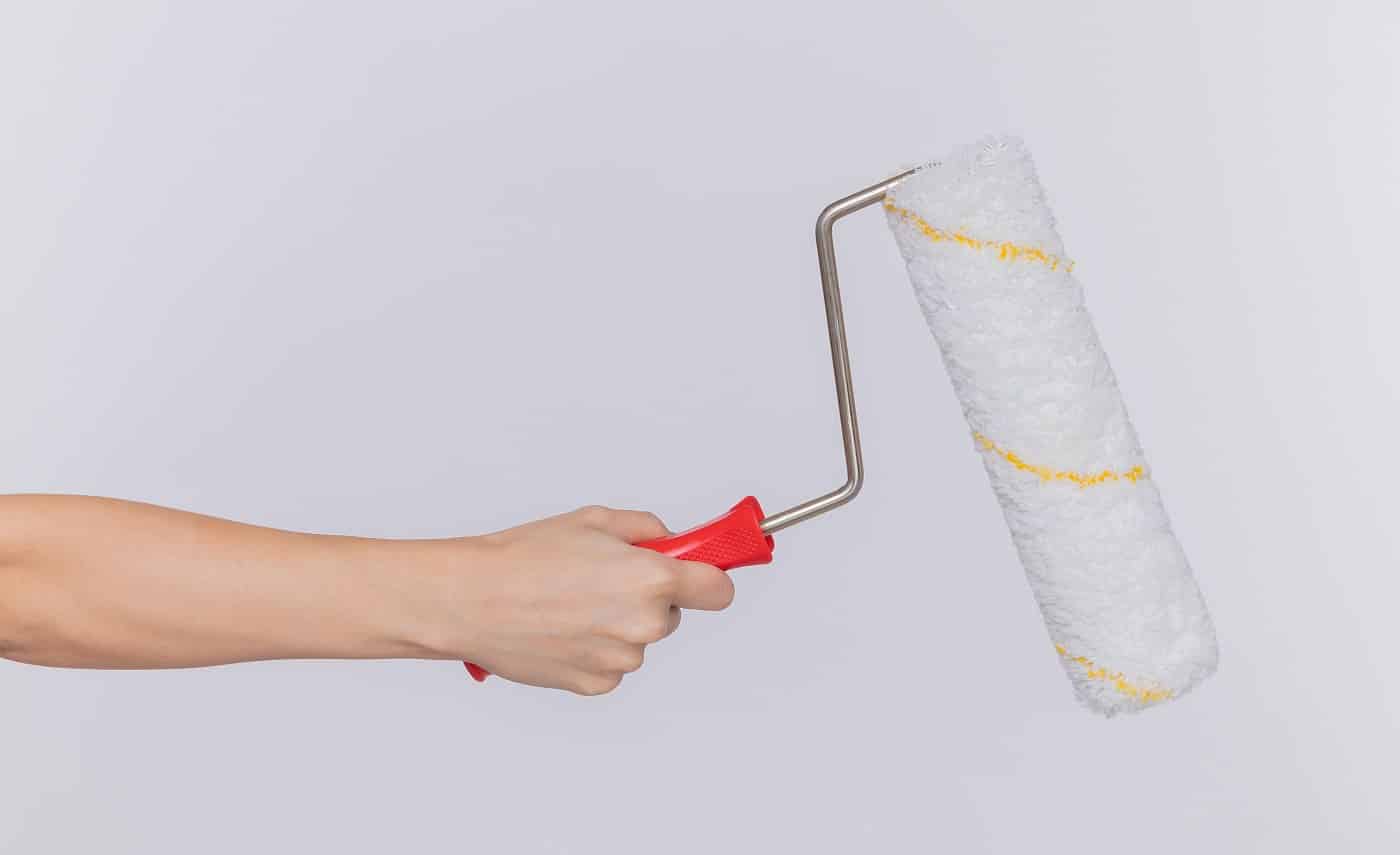 cropped photo of hand of woman holding paint roller over isolated white background