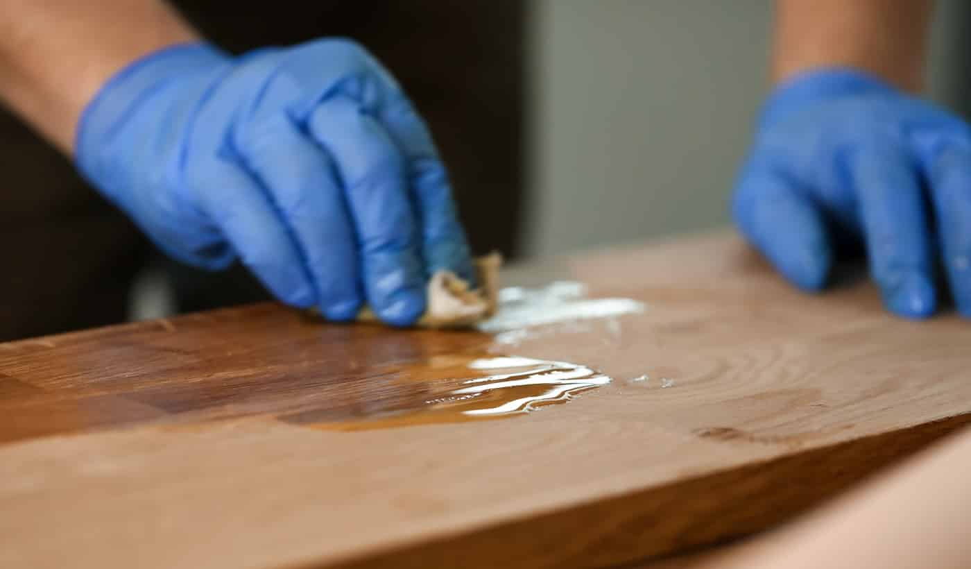 Close-up of woodworker hands in protective gloves covering wooden surface. Joiner lacquering part of furniture. Carpentry work and joinery processing concept