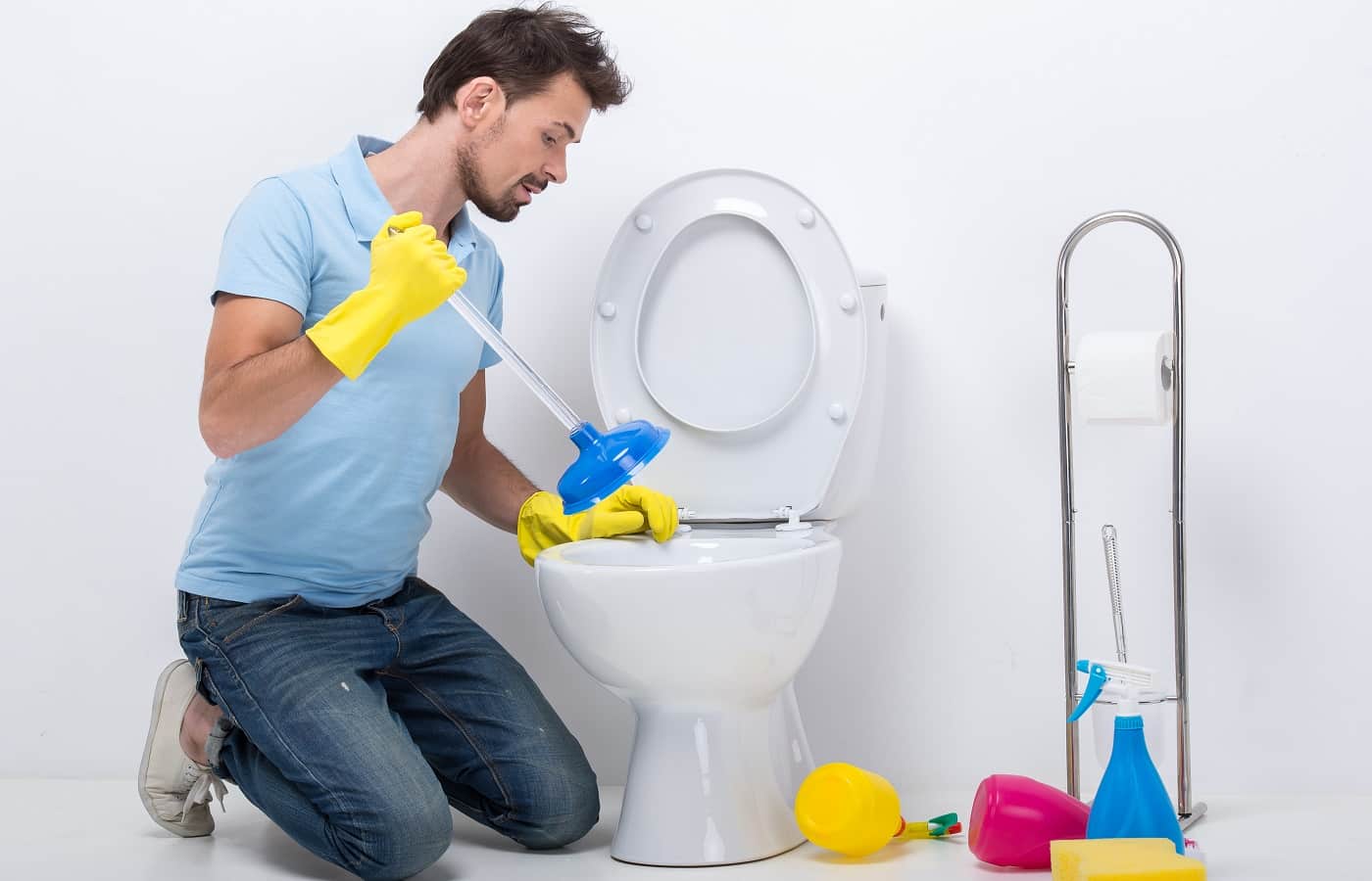 Young man unclogging a toilet with plunger.