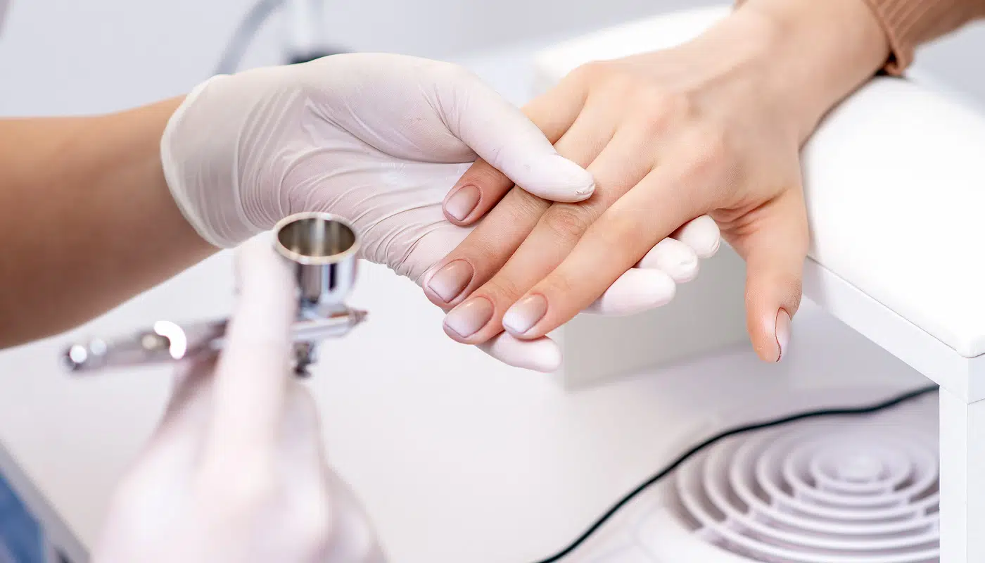 Young woman receiving manicure by airbrush in nail salon. Procedure for spraying paint on the nails. Luminess Silk