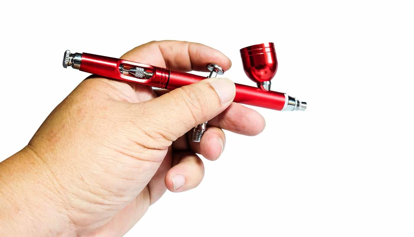 Red airbrush spray tool in hand for paintingg hobby or work for art .
