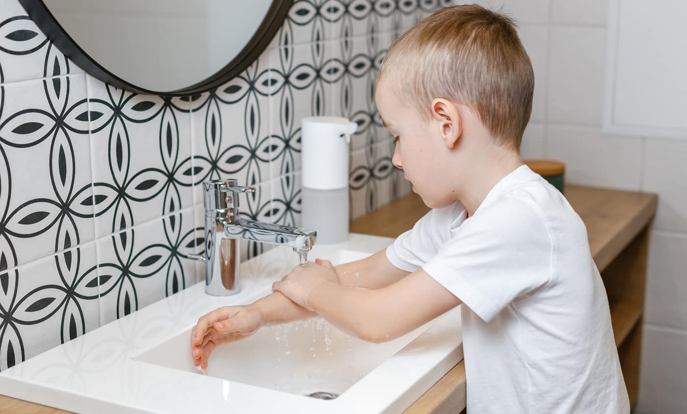 Boy washing hands in bathroom using sensor soap dispenser. Kid hygiene, healthcare and body care