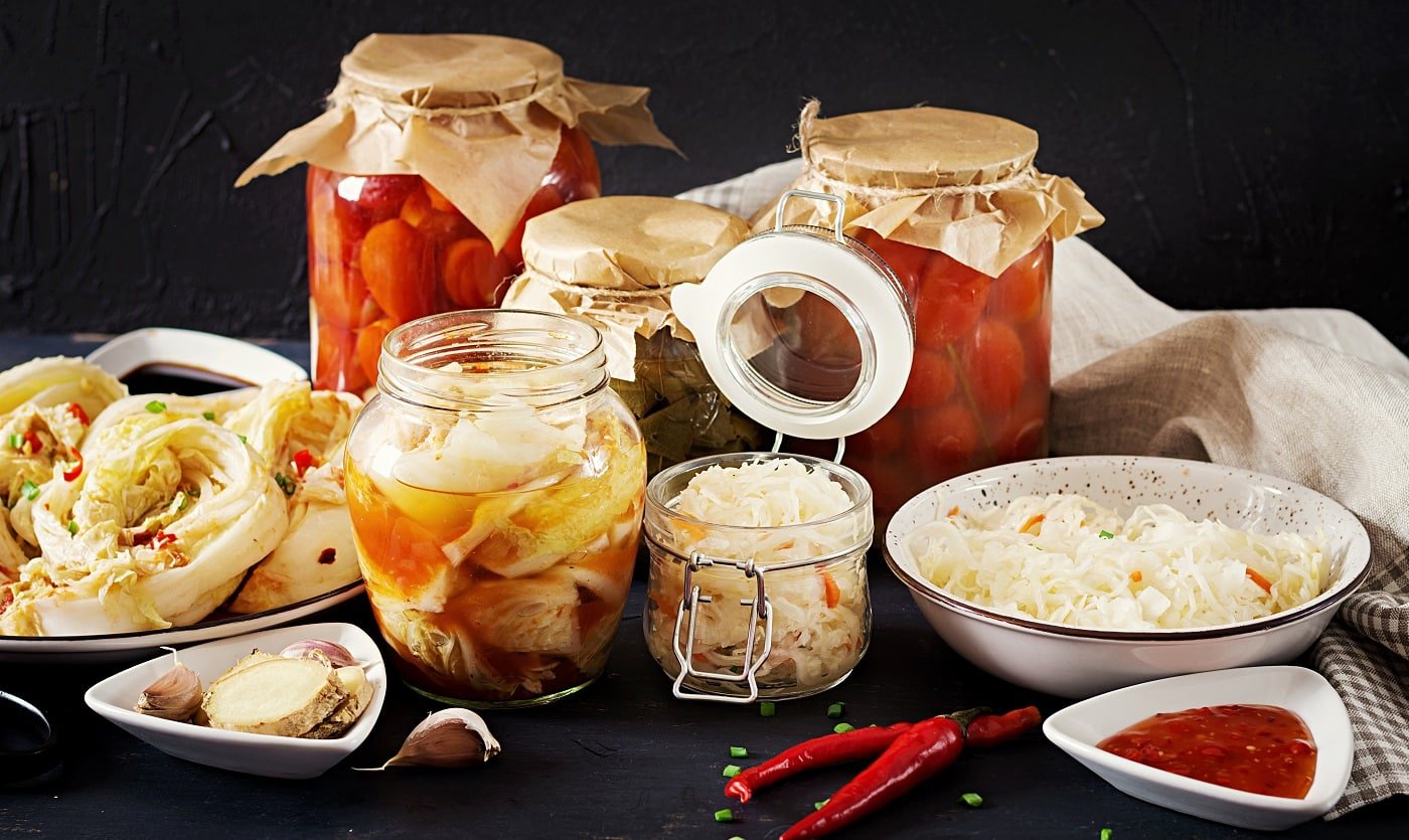 Fermented food. Vegetarian food concept. Cabbage kimchi, tomatoes marinated, sauerkraut sour glass jars over rustic kitchen table. Canned food concept. Copy space