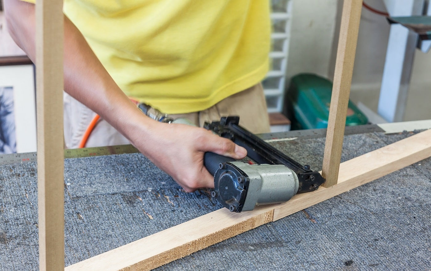 Worker using air nailer shooting nail into log for strengthen holding of wooden frame