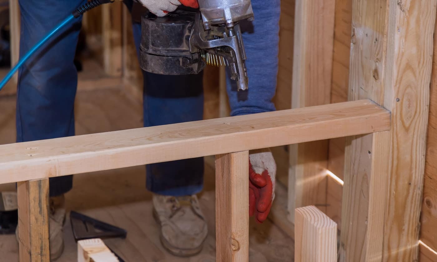 Professional carpenter holding air nail gun pneumatic framing nailer in the new home construction. Framing Nailer Buyer’s Guide