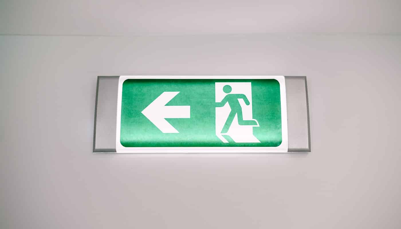 Close-up of a fire safety evacuation light sign with a running man and an arrow on the wall under the ceiling. Green exit indicator. High quality photo