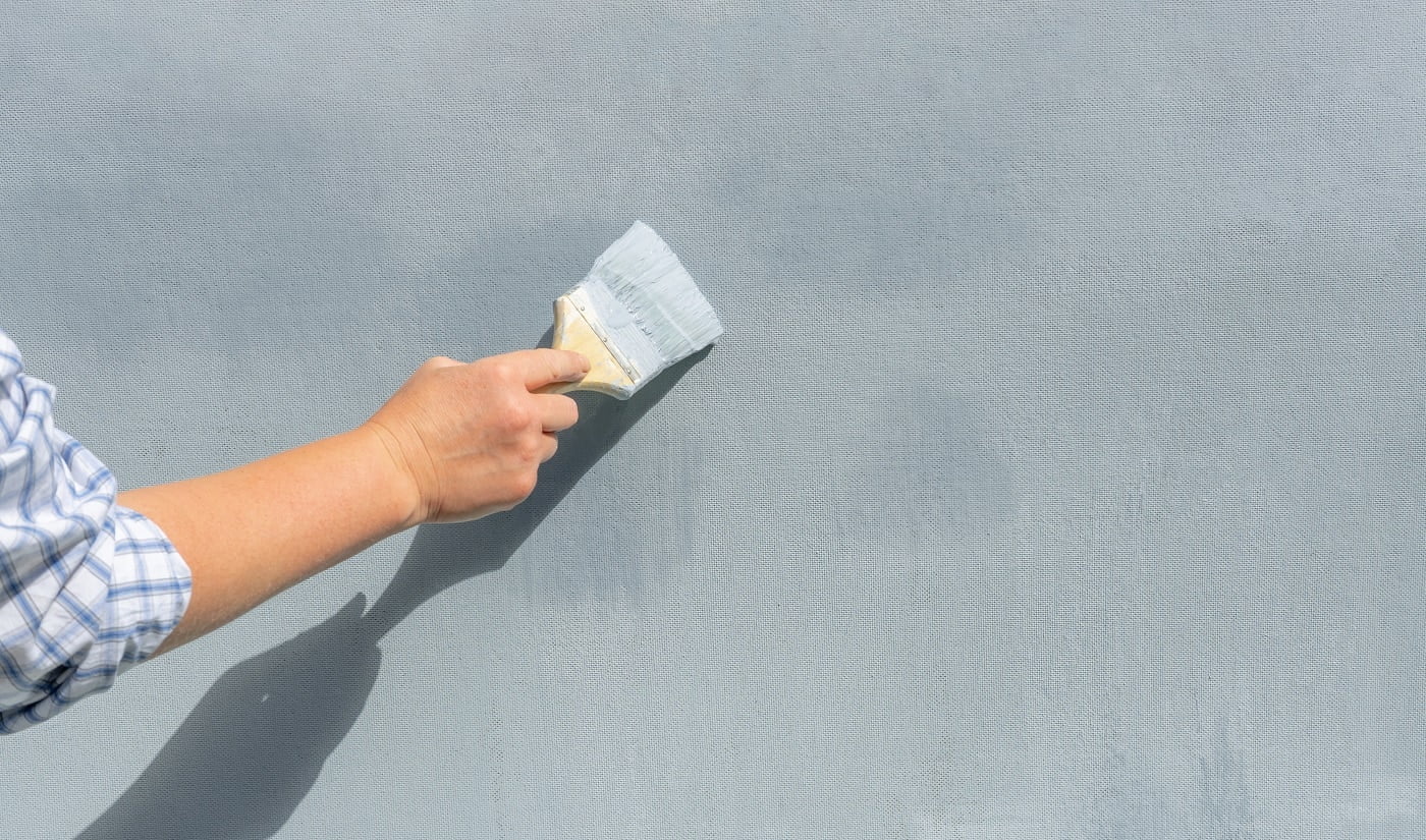 The hand of a repairman with a paintbrush paints the wall blue.