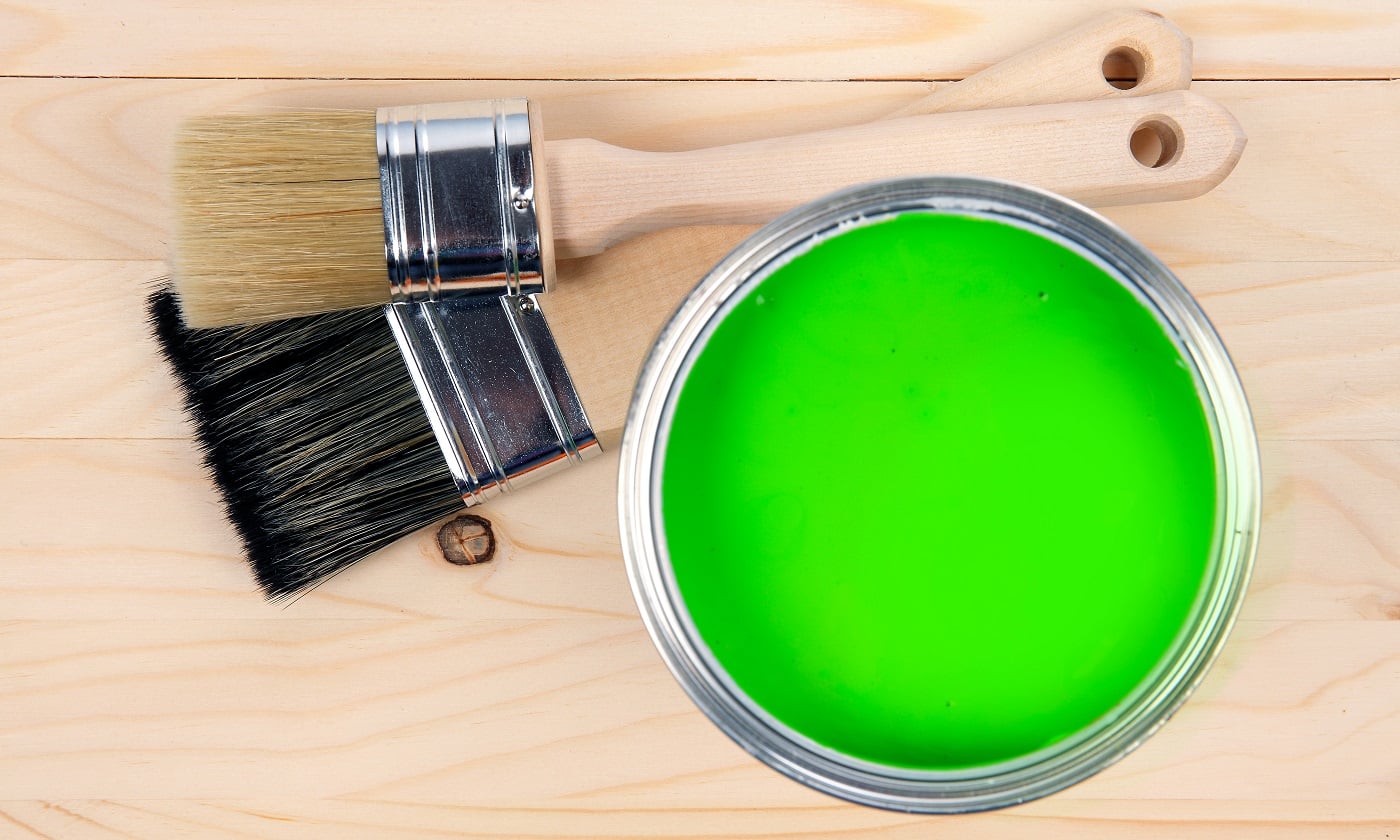 Colorful bucket of green paint with two brushes on a wooden table