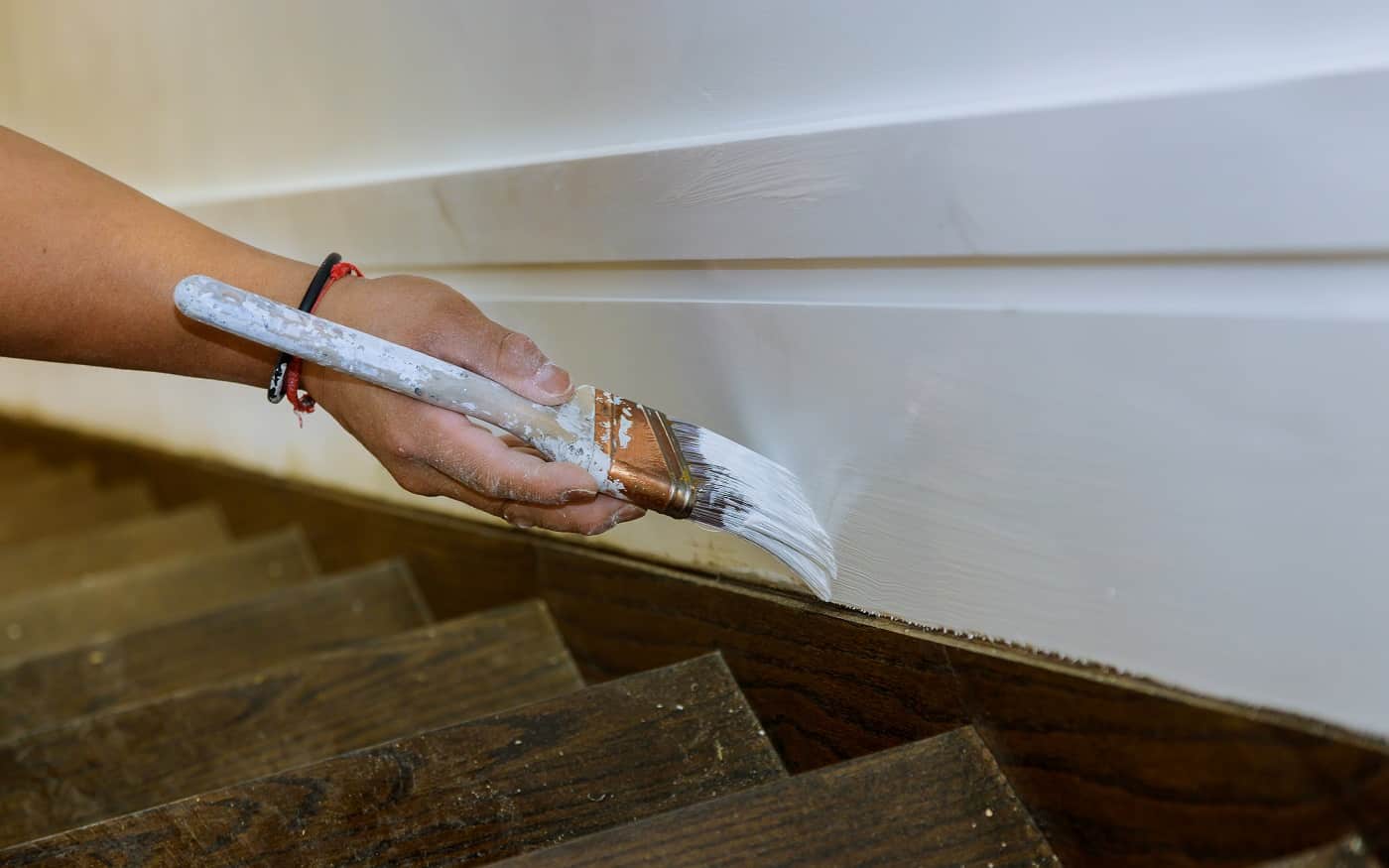 Working contractor painter hands with painting the wood molding trim on stairs with brush