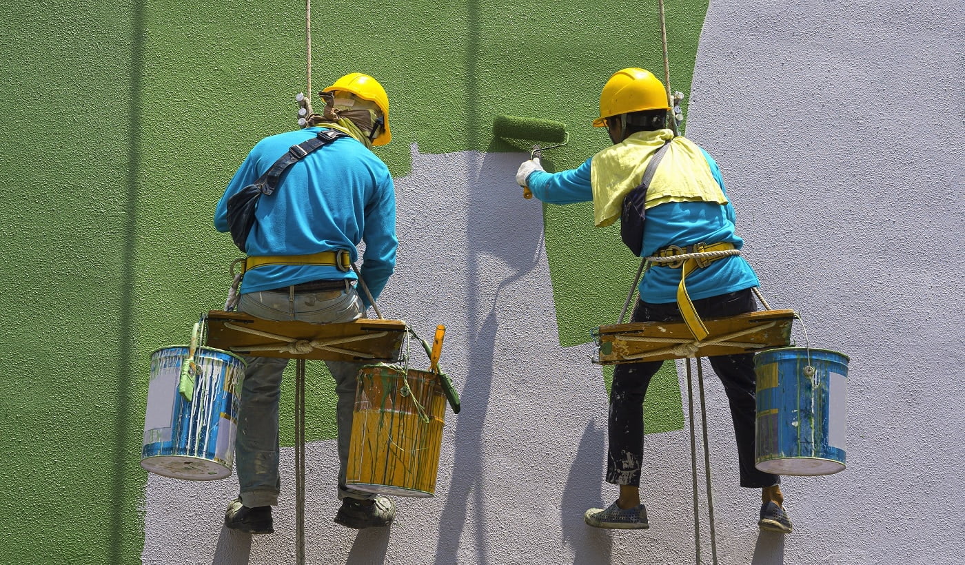 Two painters are painting the exterior of the building on a dangerous looking scaffolding hanging from a tall building.