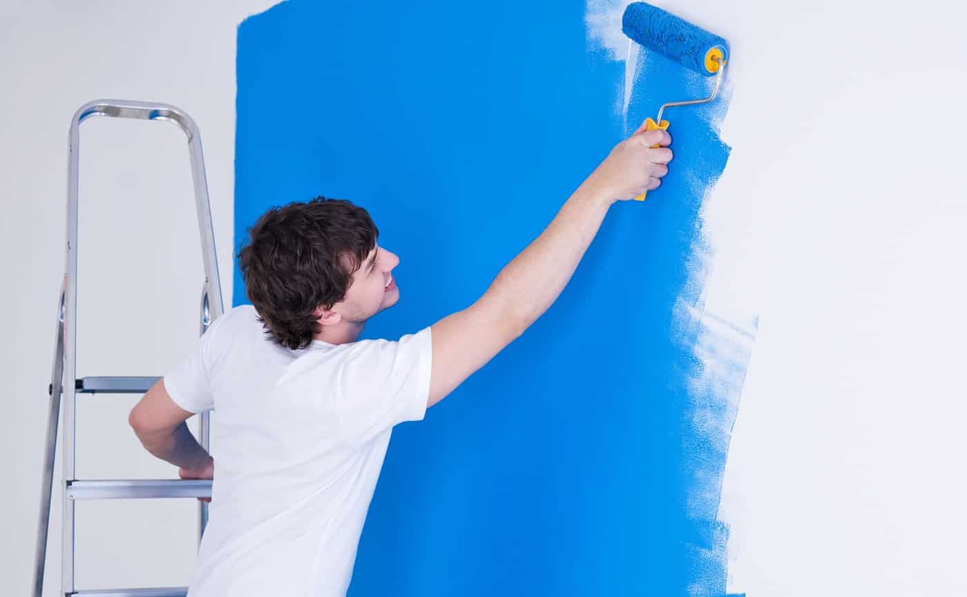 Handsome young man painting the wall in blue - horizontal