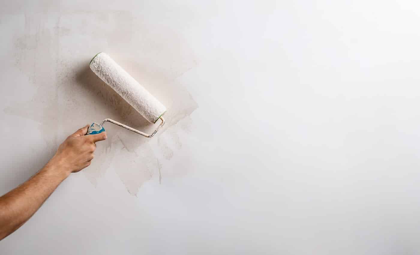 Close up photo of hand painting wall with roller in white color. Copy space.