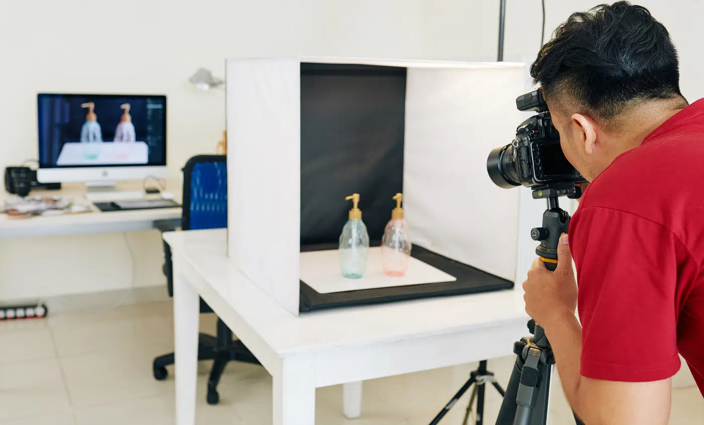 Photographer taking photos of glass bottles in light cube with black background in small studio