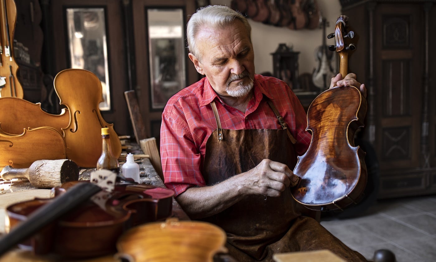 Senior carpenter craftsman polishing violin instrument in his carpenter's workshop.