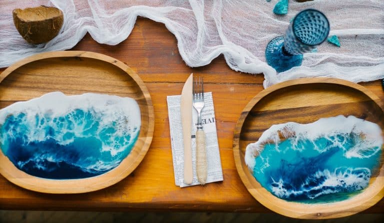 Tropical or marine style decor in the decoration of the festive table setting. Color of the year 2020, classic blue. Wooden plate with epoxy resin in the form of ocean or sea wave