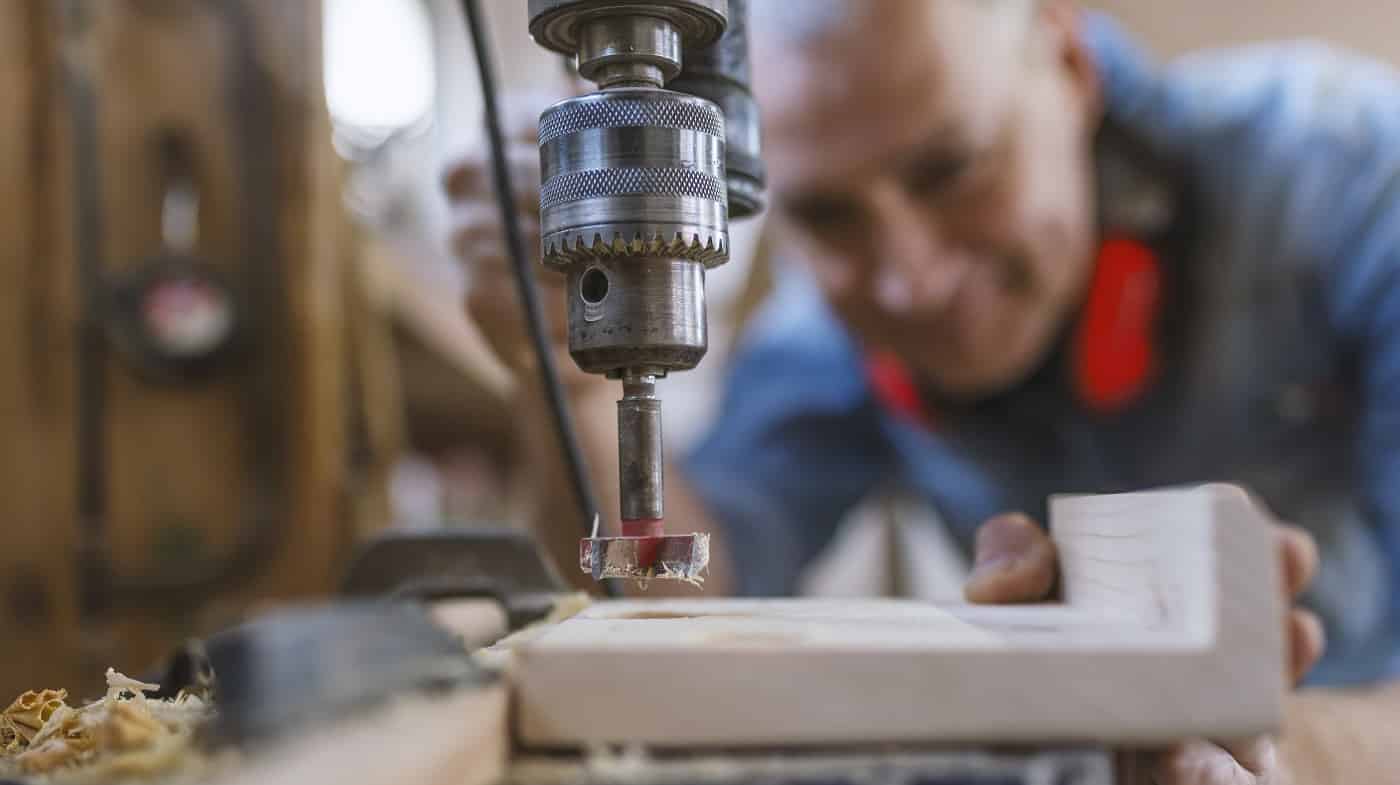 Mature carpenter using drill press in workshop. Wood working. Carpentry workshop routine. Engineer in workshop