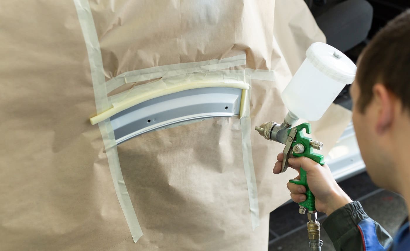 Close-up of a spray gun with white paint for painting a car in a special booth.