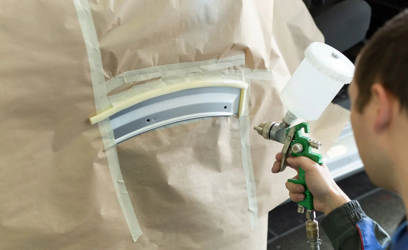Close-up of a spray gun with white paint for painting a car in a special booth.