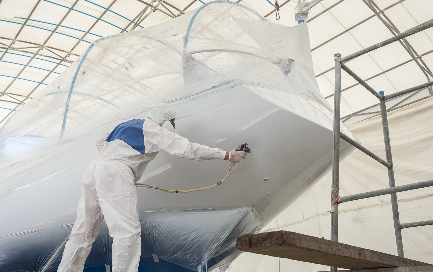 Worker wearing protective uniform and spraying paint to the boat