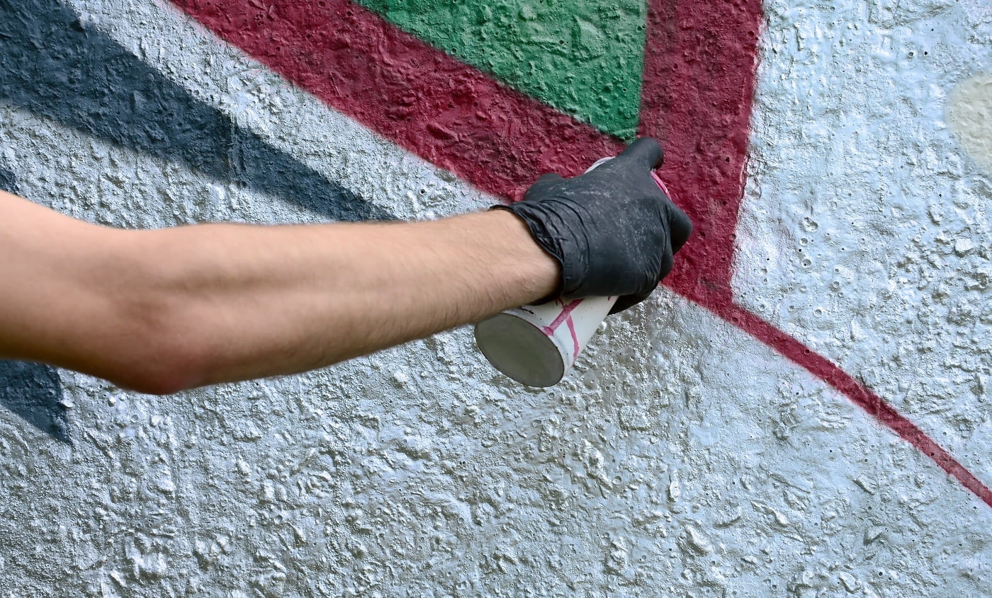 A hand in black gloves paints graffiti on a concrete wall. Illegal vandalism concept. Street art.