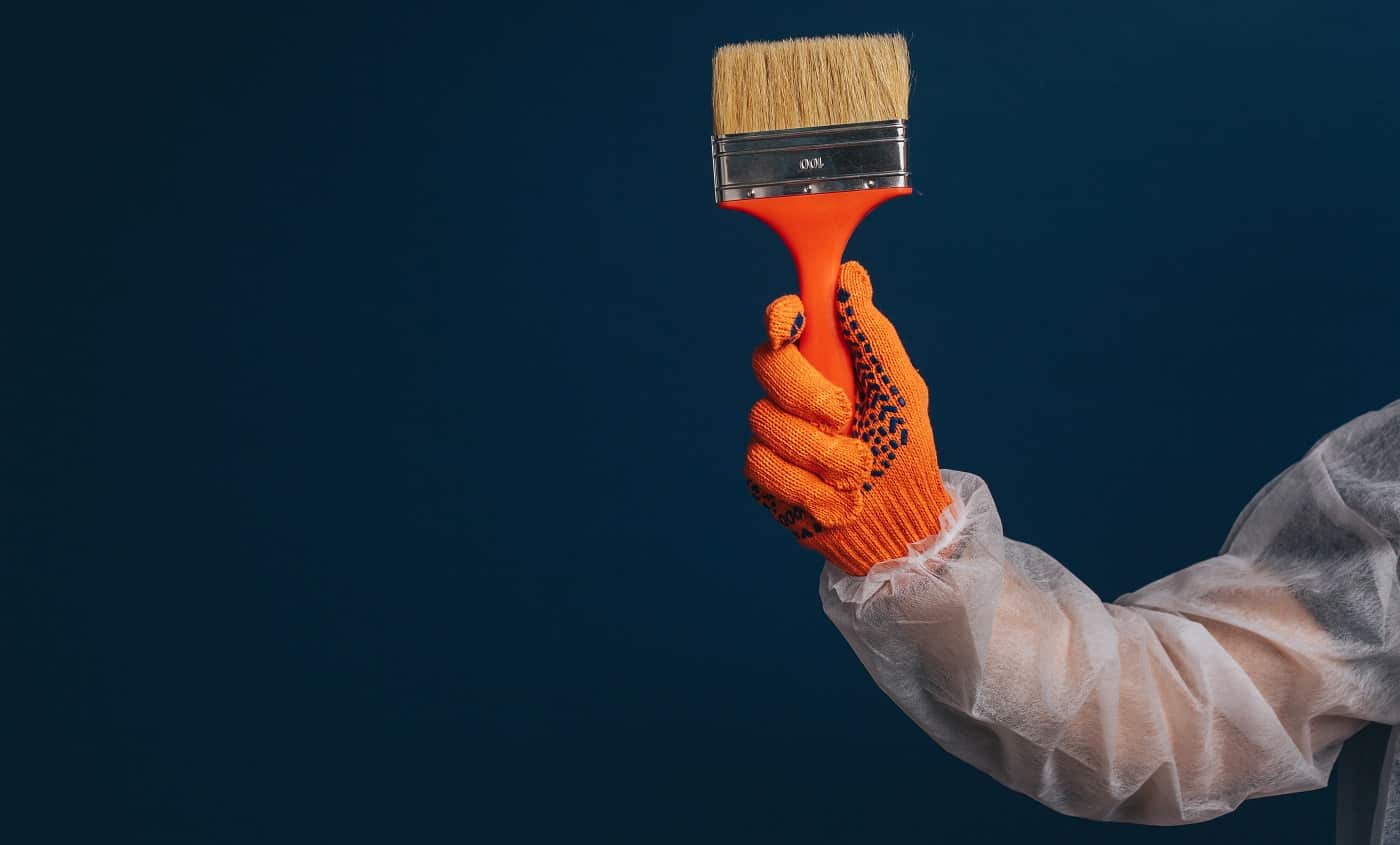 Builder's hand is holding paint brush, isolated over blue background.