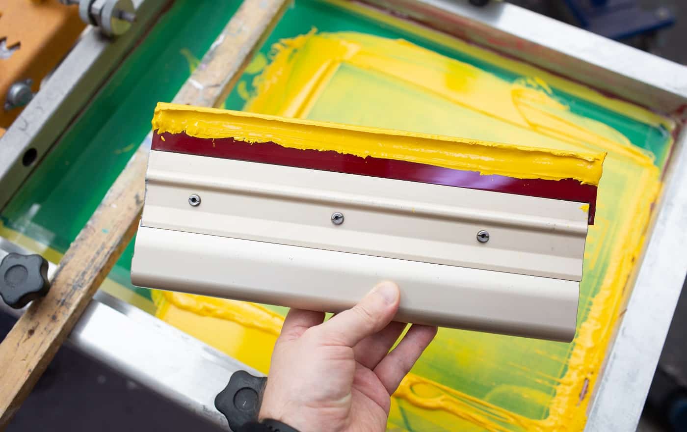 Squeegee for Serigraphy silk screen print process at clothes factory. Frame, squeegee and plastisol color paints.