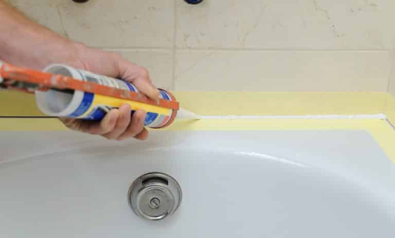 Worker puts Best Caulk For Your Showers and Bathtubs the joint between tub and wall.