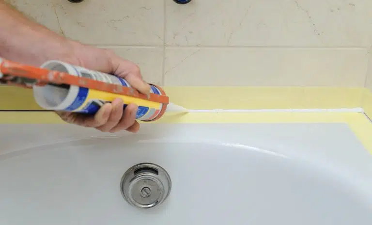 Worker puts Best Caulk For Your Showers and Bathtubs the joint between tub and wall.