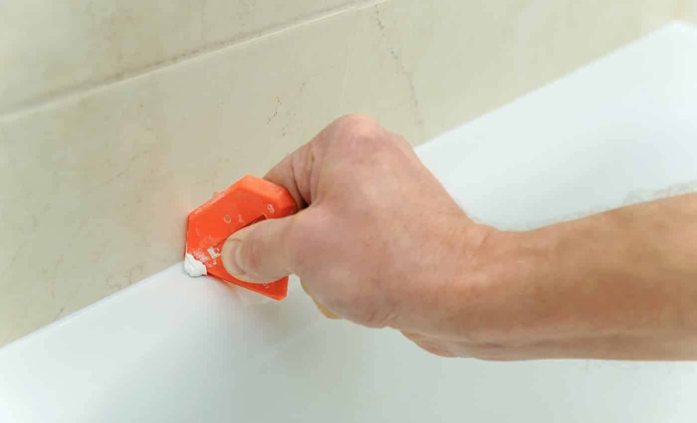 Worker smoothing silicone sealant between the bath and the wall using a spatula.