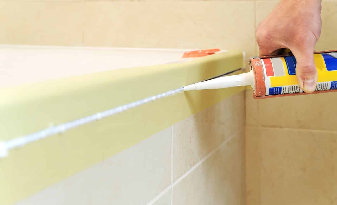Worker puts silicone sealant to caulk the joint between tub and wall.