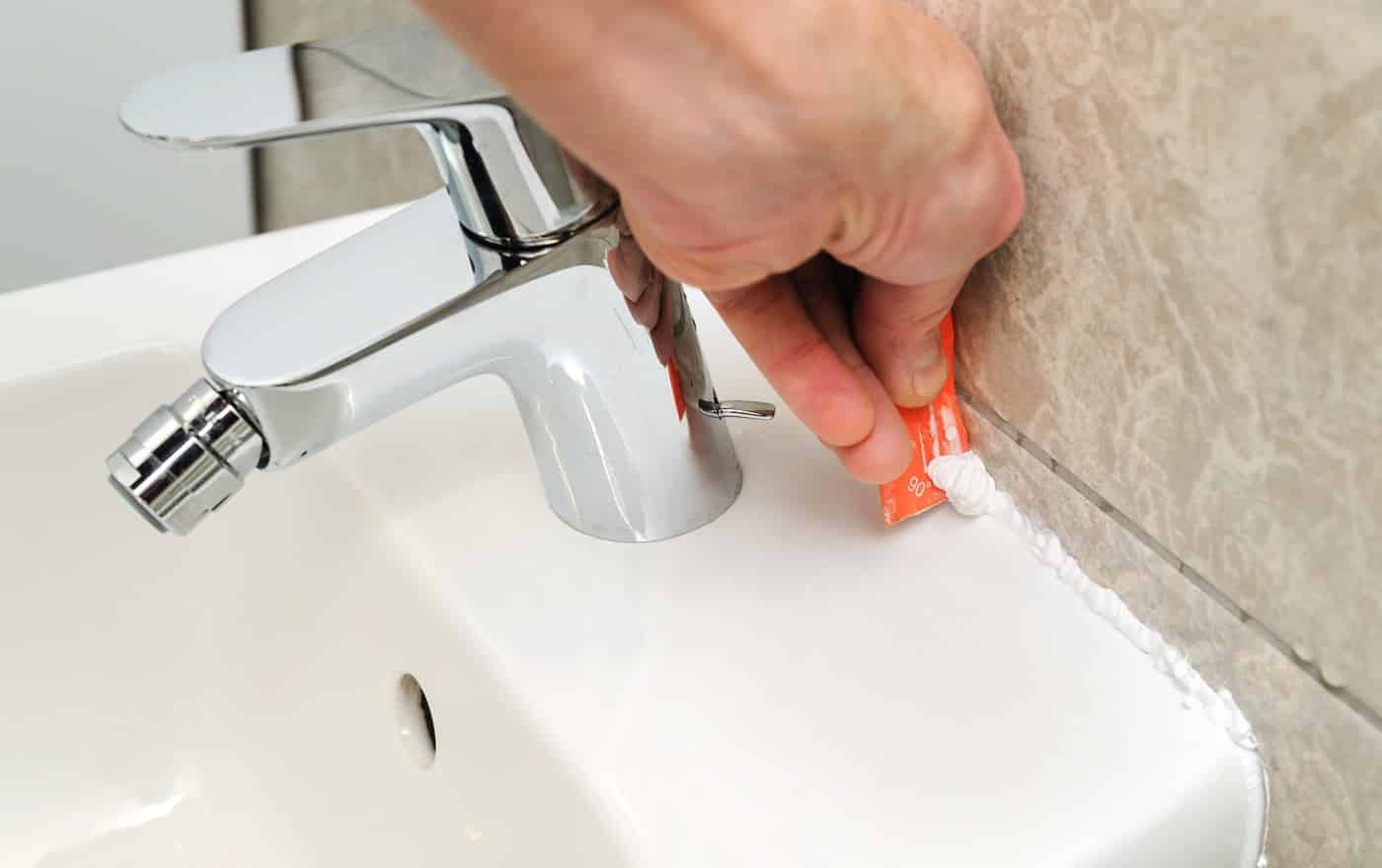 Worker smoothing silicone sealant between the bidet and the wall using a spatula.