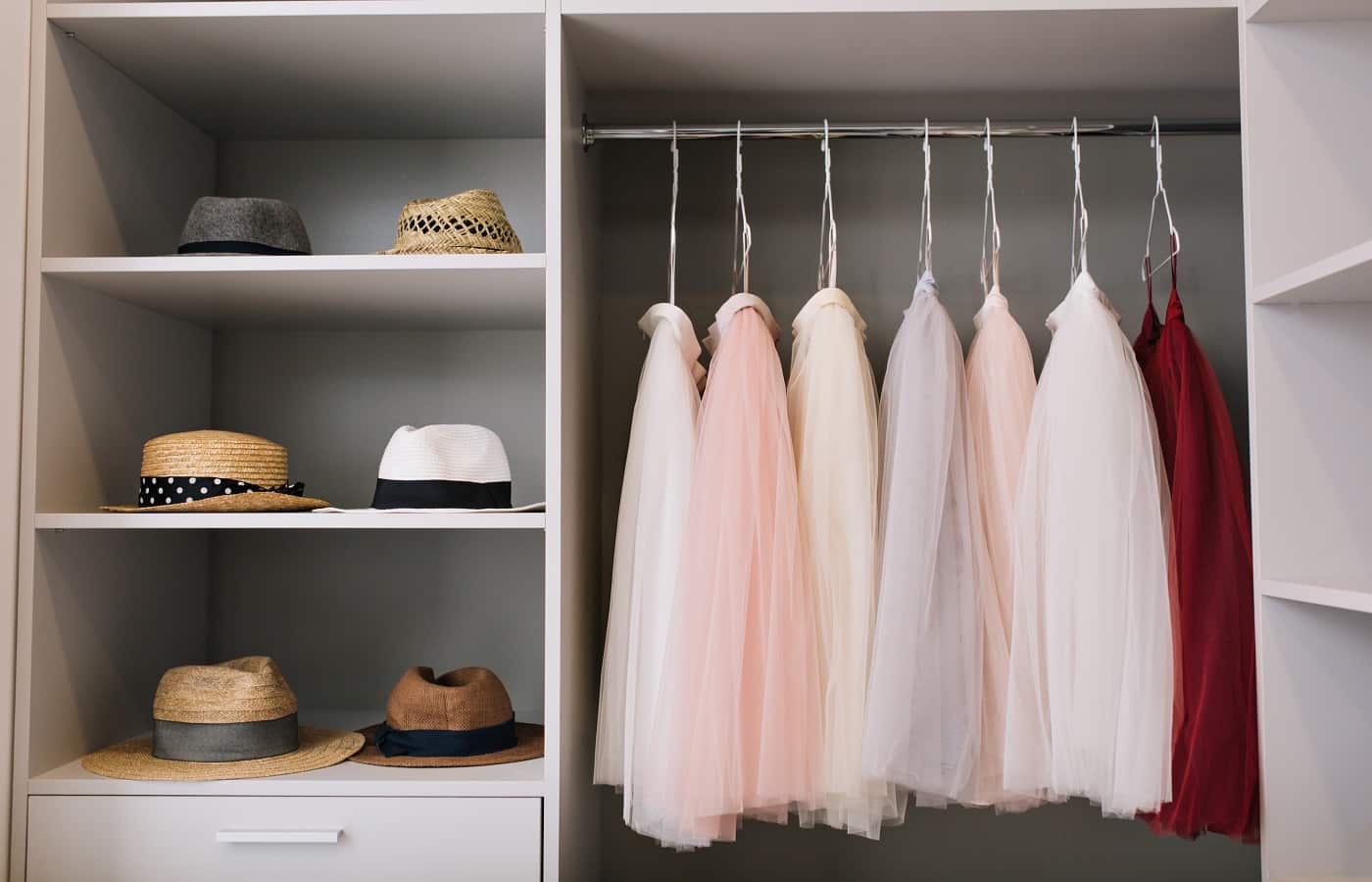 Modern bright dressing room with shelves. Fashionable hats, beautiful pink and red dresses hanging in wardrobe