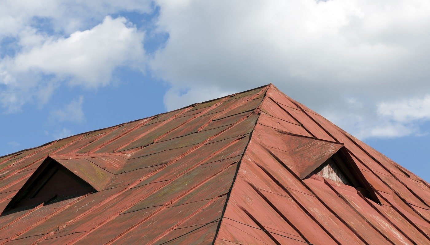 old red metal roof of the building against the blue sky, a lot of damage on the metal, closeup