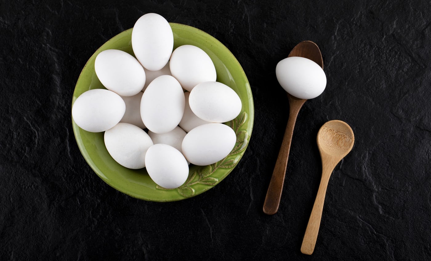 Bunch of raw eggs on green plate with wooden spoons. High quality photo
