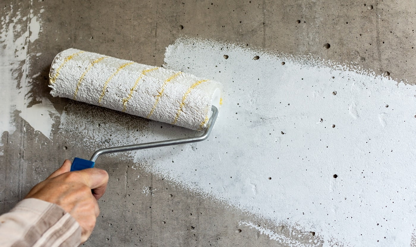 A painter paints a concrete wall with white paint, a male hand with a paint roller for painting a wall