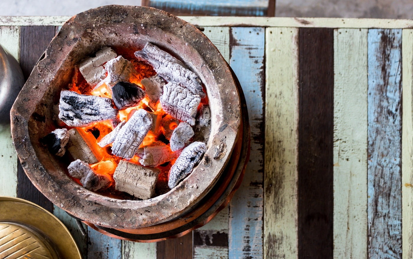 Burning charcoal with flame in the baked clay stove on the wooden table