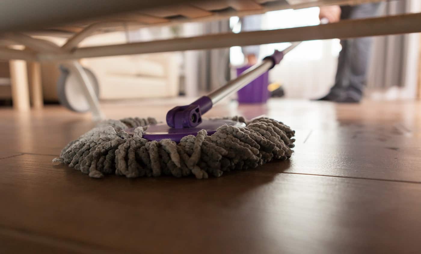 Guy mopping the dust under sofa in apartment.