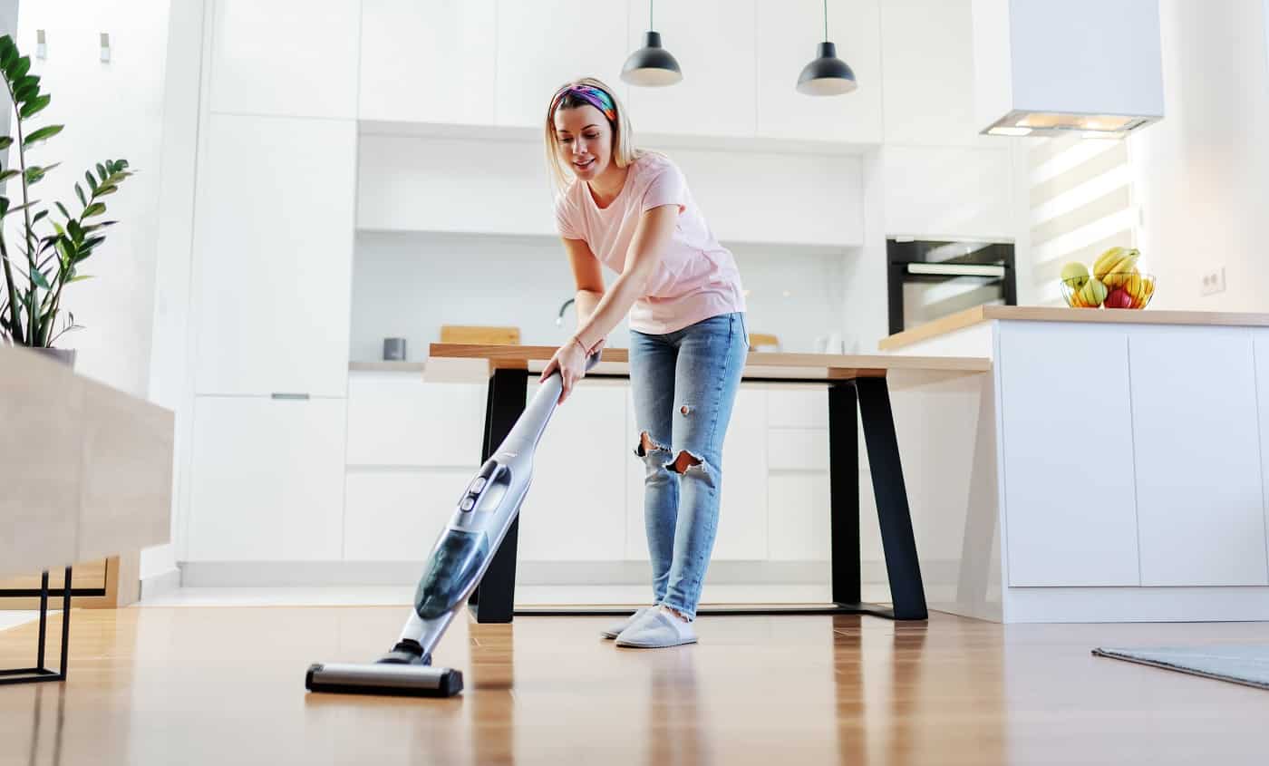 Full length of worthy caucasian blonde housewife using steamer to clean floor in living room.